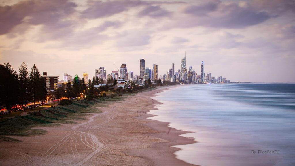 Sunset over Broadbeach with golden sand, gentle surf, and the Gold Coast skyline glowing under pastel skies, Queensland.
