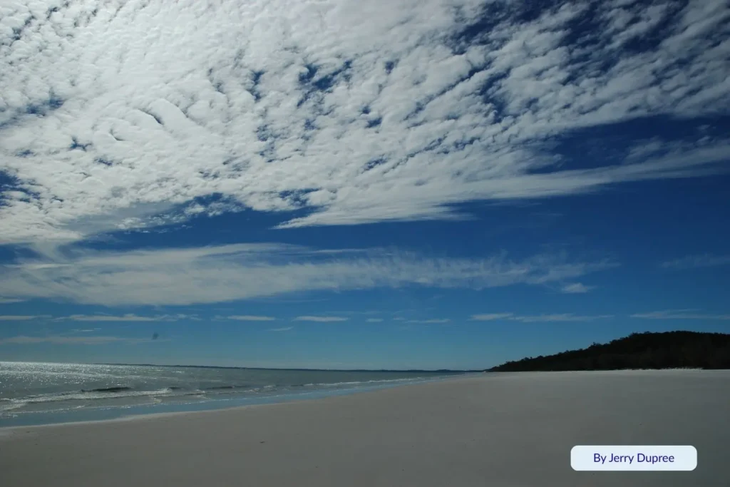 Wide view of Platypus Bay’s pristine white sand and calm blue water under scattered clouds on Fraser Island (K’gari), Queensland.